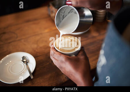 African barista making a cappuccino in a cafe Stock Photo