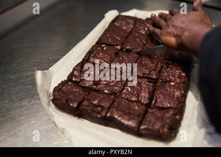 Baker cutting brownies into squares in a cafe kitchen Stock Photo
