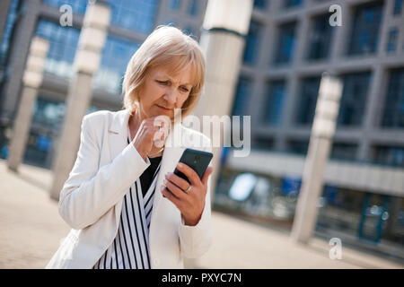 Outdoor portrait of worried senior businesswoman who is using smartphone. Stock Photo