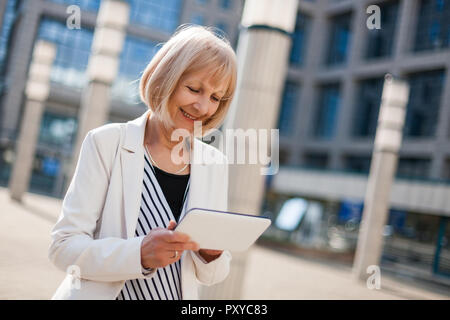 Outdoor portrait of happy senior businesswoman who is using digital tablet. Stock Photo