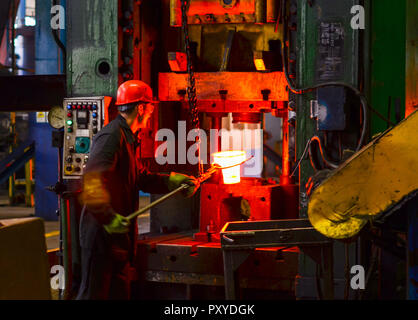 Hot iron in smeltery held by a worker. High precision hot forging product, automotive part production by hot forging process, automatice line hot forg Stock Photo