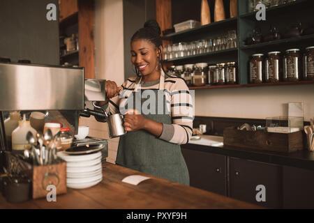 Smiling young African barista frothing milk behind a cafe counter Stock Photo