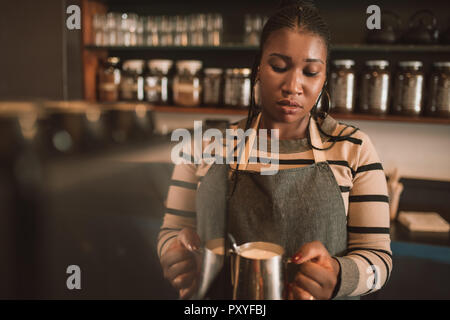 Young African barista making a cappuccino behind her cafe counter Stock Photo