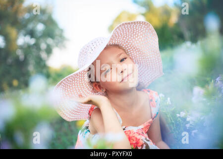 Beautiful girl in a pink hat in summer in a green garden among flowers. Stock Photo