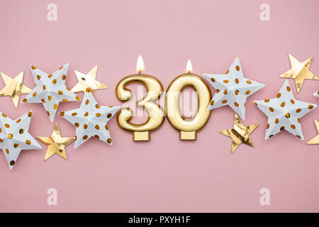 Number 30 gold candle and stars on a pastel pink background Stock Photo