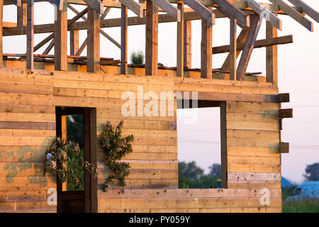 Detail view, corner of new wooden ecological traditional cottage of natural lumber materials with steep roof frame under construction in green neighbo Stock Photo