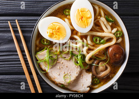 Spicy udon noodle soup, pork, boiled eggs, shiitake and onions close-up in a bowl on the table. horizontal top view from above Stock Photo