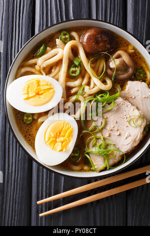 Traditional Japanese udon noodle soup with pork, boiled eggs, mushrooms and green onions closeup in a bowl on the table. Vertical top view from above Stock Photo