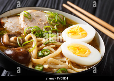 Spicy udon noodle soup, pork, boiled eggs, shiitake and onions close-up in a bowl on the table. horizontal