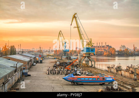 Sunset in old harbor. Portal cranes and high-speed hydrofoil ship. Stock Photo