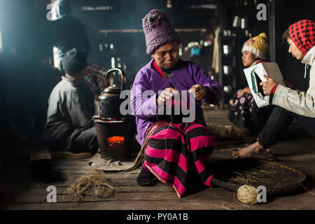 Elderly woman wearing knit hat knitting indoors in small rural house, Myanmar, Shan, Myanmar