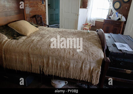 Antique bed cover on bed with pillows & old  rustic wooden trunk at foot of bed. Interior of home at Chestnut Square Historic Village, McKinney Texas. Stock Photo