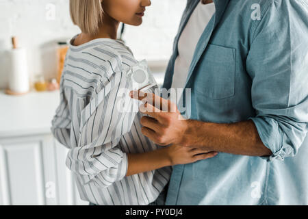 cropped image of boyfriend hugging girlfriend and holding condom in kitchen Stock Photo