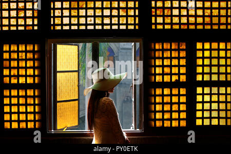 Woman in white lace dress and hat in hallway in front of capiz (shell) window in San Agustin Church, Manila, Philippines Stock Photo