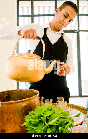 Waiter holding large kettle pouring tea into glasses, Madaba Governorate, Jordan Stock Photo