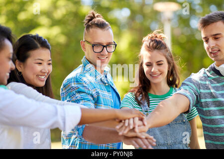 happy smiling friends stacking hands in park Stock Photo