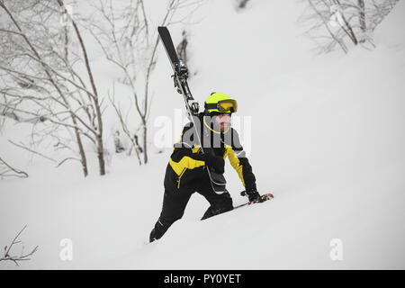Happy smiling skier walks in the mountains in deep snow after freeride alpine skiing with ski on shoulder Stock Photo
