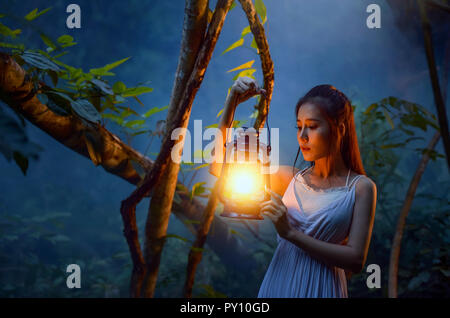 Woman standing in forest holding a lantern, Thailand Stock Photo