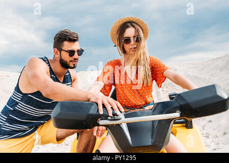 handsome young man teaching his girlfriend how to ride atv in desert Stock Photo