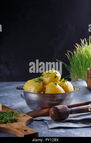 Hot boiled potatoes in a plate dusted with greens and smoke on a gray background. Stock Photo