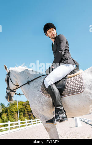 side view of handsome male equestrian sitting on horseback at horse club Stock Photo