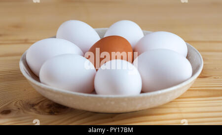 One brown and white eggs in a ceramic dish on a wooden table. Stock Photo