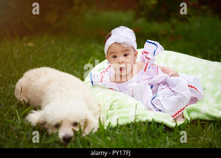 Small baby girl with white poodle dog sit on green grass background Stock Photo