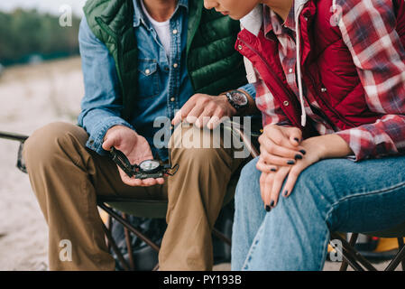 cropped shot of couple with compass sitting on chairs on camping Stock Photo
