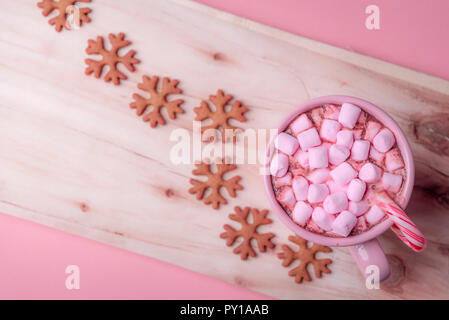 Winter sweets in pink shades, a cup of hot chocolate with mini marshmallows and a Christmas candy cane and snowflakes shaped gingerbread cookies. Stock Photo