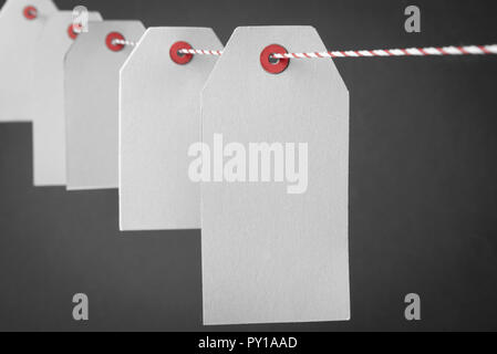 Blank paper tags aligned on a red-white rope against a gray background Stock Photo
