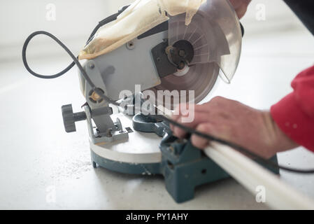 Laborer using a small electric circular saw to cut a length of plastic profile with focus to the power tool. Stock Photo