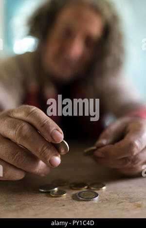 Concept of poor man with dirty hands counting coins at old wooden table. Stock Photo