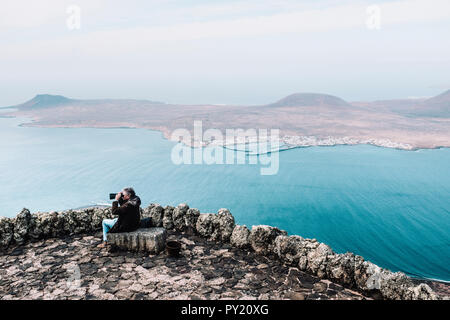 Man looking through binoculars at landscape with Isla de La Graciosa from viewpoint at Mirador del Rio, Lanzarote, Canary Islands, Spain Stock Photo