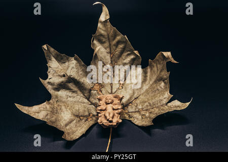 Baby Jesus Christ in the manger on a dry leaf isolated on black background. Christmas Nativity Scene figure. Stock Photo