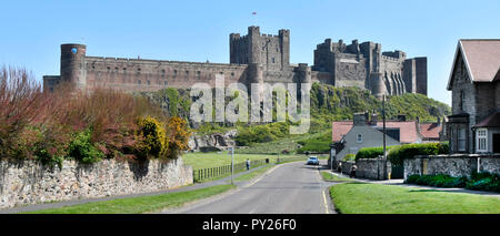 Road out of Bamburgh village panoramic landscape & dramatic backdrop of historical Bamburgh Castle on coast of Northumberland North East England UK Stock Photo