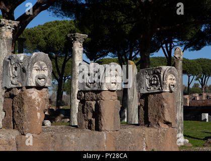 Three stone actors masks in the ancient theatre of Ostia Antica. The stone masks are on stone pedestals and are brightly lit in the morning winter sun Stock Photo