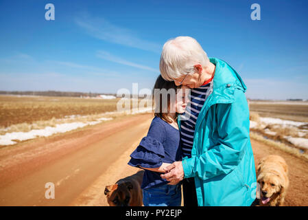 Grandmother standing by a road with two dogs hugging her granddaughter, United States Stock Photo