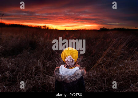 Rear view of a girl standing in a field watching the sunset, United States Stock Photo