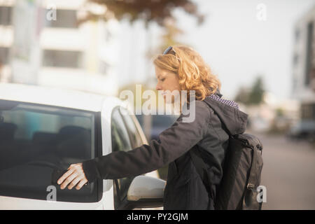 Woman standing by a car opening the door with her mobile phone Stock Photo