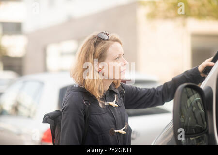 Woman standing by a car opening the door with her mobile phone Stock Photo