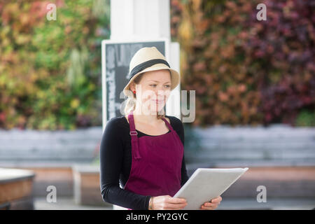 Portrait of a smiling waitress in an outdoor restaurant holding menus Stock Photo