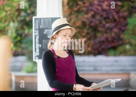 Portrait of a smiling waitress in an outdoor restaurant holding menus Stock Photo