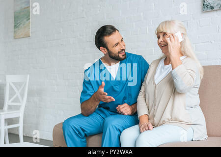 smiling male nurse looking at happy senior woman talking by smartphone Stock Photo