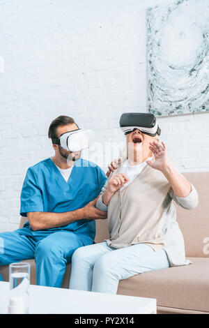 young social worker and excited senior woman using virtual reality headsets Stock Photo
