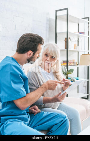 shocked senior woman looking at social worker pointing with finger at digital tablet Stock Photo