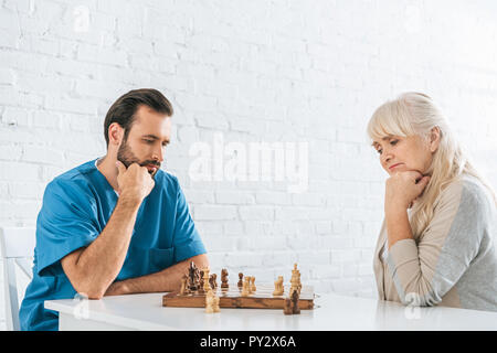 concentrated senior woman and young social worker playing chess together Stock Photo