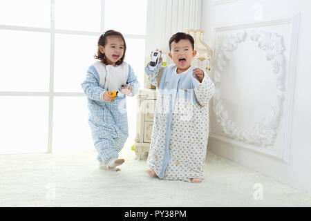 the sibings wearing baby bear sleeping bags are playing hide and seek Stock Photo