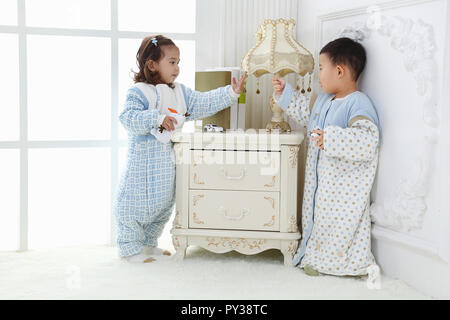 the sibings wearing baby bear sleeping bags are playing hide and seek Stock Photo