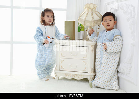 the sibings wearing baby bear sleeping bags are playing hide and seek Stock Photo