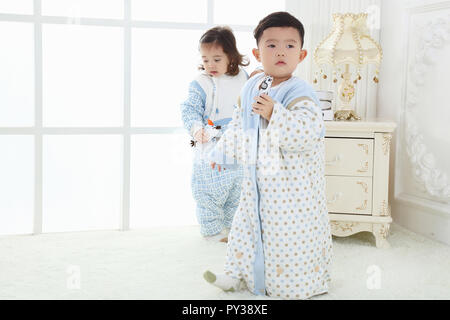 the sibings wearing baby bear sleeping bags are playing hide and seek Stock Photo